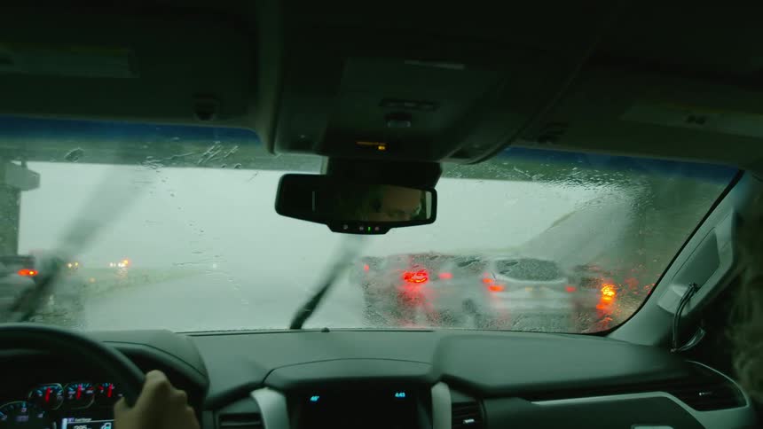 Many cars stop on the side of the highway with their hazard lights flashing and the camera vehicle passes by in heavy rain and hail as the wipers struggle to clear the rain