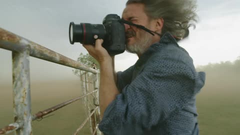 Extreme winds nearly knock over an adventurous storm chaser man as he documents a supercell thunderstorm in tornado alley