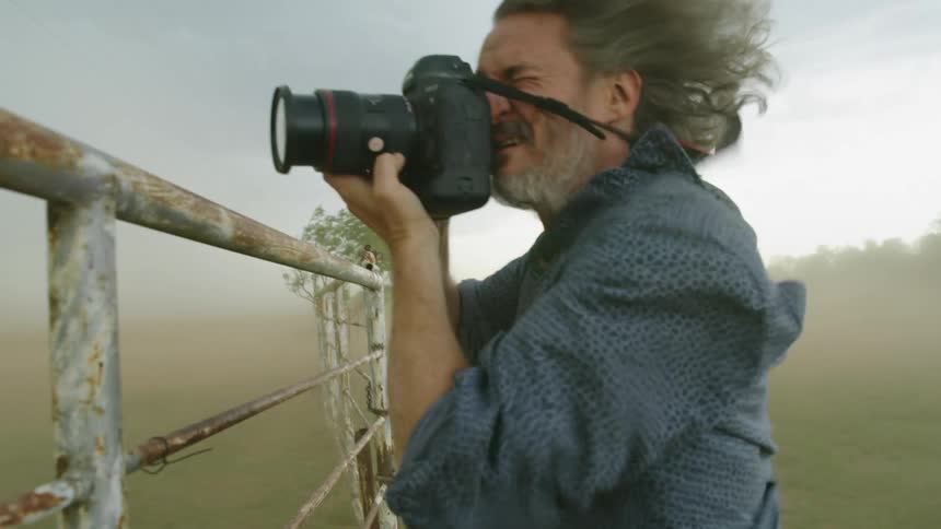 Extreme winds nearly knock over an adventurous storm chaser man as he documents a supercell thunderstorm in tornado alley