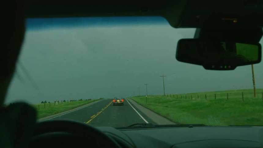 Slow motion shot of a strong bolt of lightning striking straight down the road the cars are driving on just before the wiper blades clear the rain