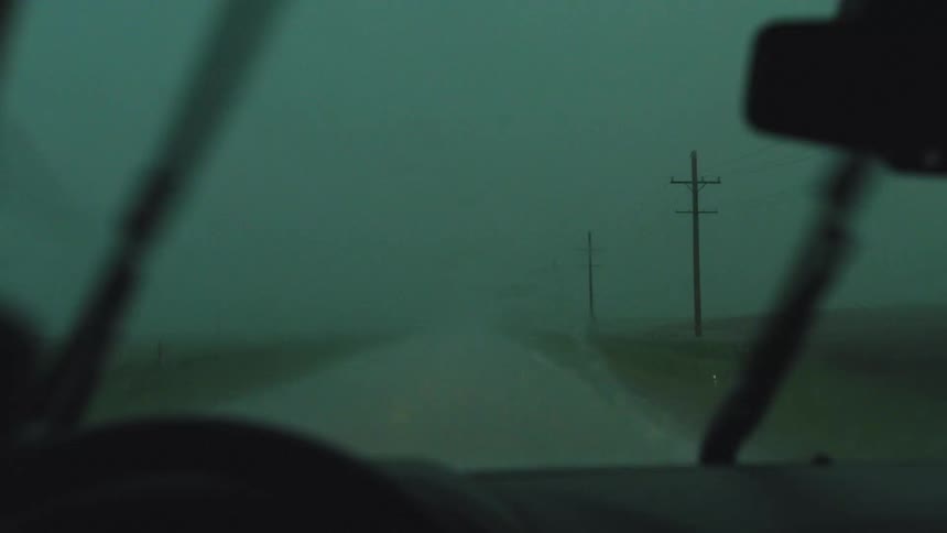 A car drives down a remote road during a severe storm with rain and the windshield wipers struggling to clear the heavy rainfall