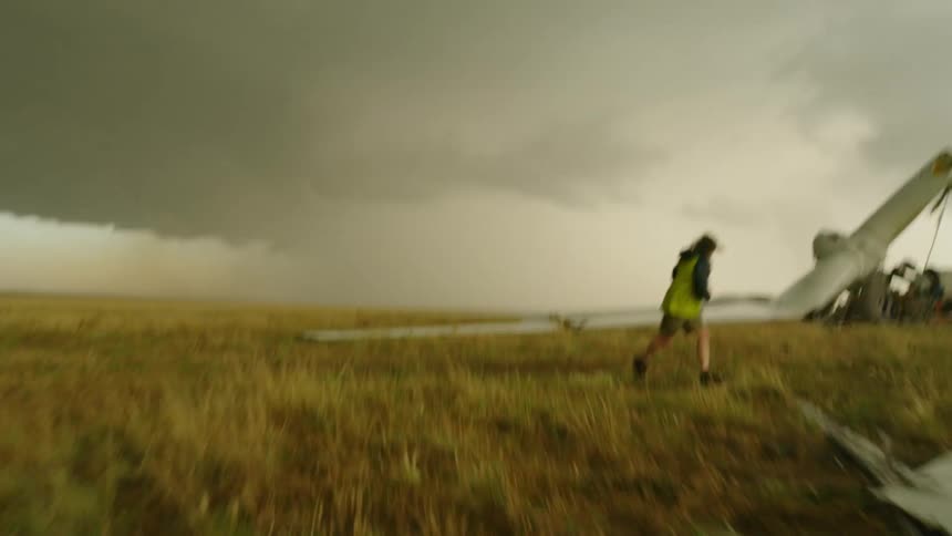 A tornado struck a windmill at a wind farm and a man runs as fast as possible to inspect the scene and jumps one of the broken windmill blades