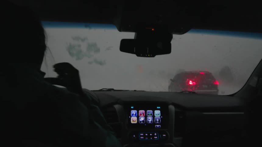 Extreme hail pounds cars as a female driver passes another car pulled off the road awaiting the intense storm to clear