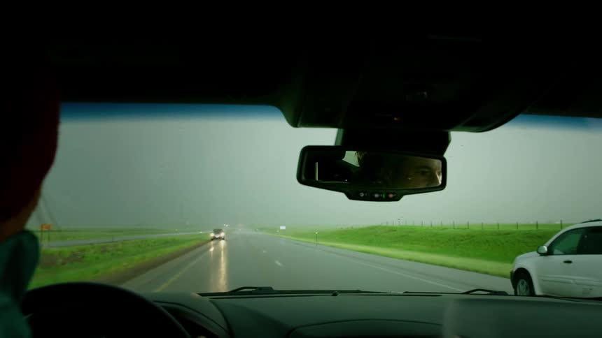 A female driver throws his hand up as a vehicle passes by him driving the wrong way on the shoulder of a rural highway in the rain
