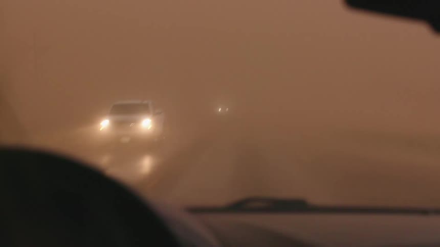 A Haboob and and dust storm obscures the daytime sky with intense darkness as cars with headlights on navigate the intense moment