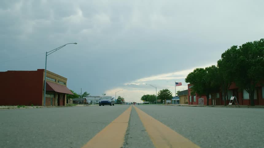 Center framed shot looking down the painted yellow line with an American flag, mammatus clouds and a rural town in the frame