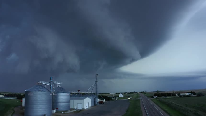 Aerial shot looking up while lowering down showing steel grain silos and the massive and intense Imperial Nebraska Mothership severe thunderstorm supercell once in a lifetime shot