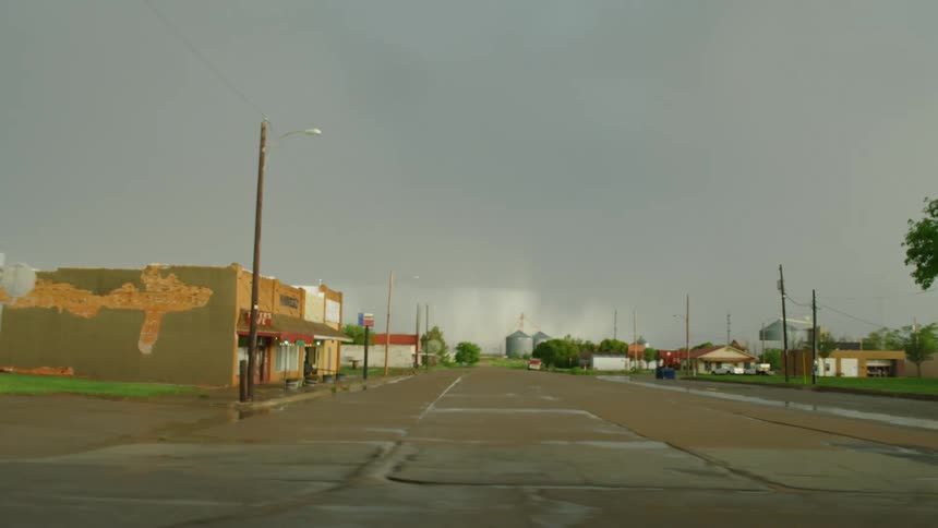 Shot out the window of a moving car (drivers perspective) of a rural town and old buildings when a massive bolt of lightning strikes the ground on the far end of town