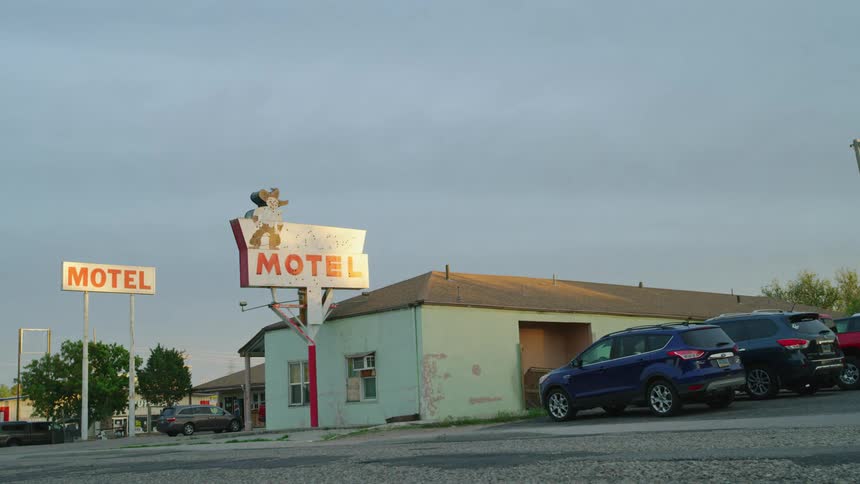 Time lapse of an old motel sign in small town USA as storm clouds move quickly by in the background, cars and people can be seen moving in the foreground