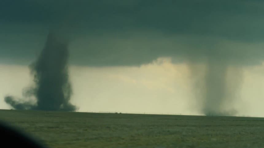 Passenger in a car POV looking out the wind shield at two tornados during a storm chasing bucket list tour to witness the power and intensity of a tornado in real life