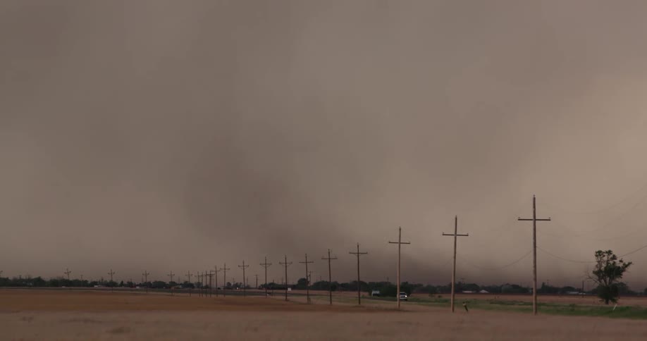 Real time shot of power lines alongside a rural highway as severe winds blow debris high into the atmosphere