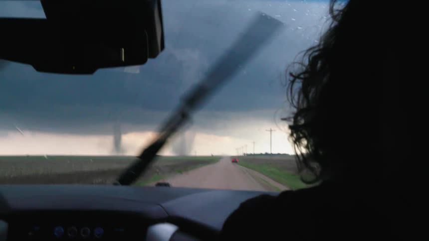 Looking out the windshield of a car at two tornados while storm chasing driving down a dirt road