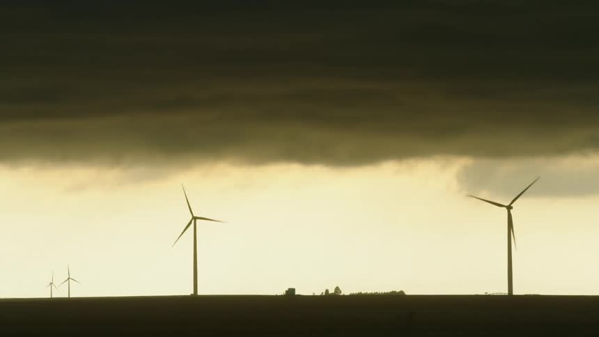 Real time shot of wind turbines spinning and generating electricity with heavy and intense storm clouds on the horizon