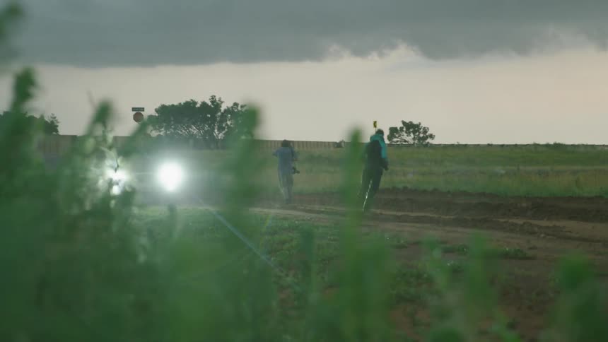 Real time shot of two storm chasers running towards the parked vehicle as large hail and strong winds overcome the landscape