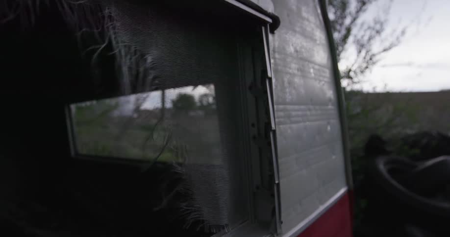 Broken screen door blowing in the wind on the side of a red and white camper trailer as a severe storm blows into the area
