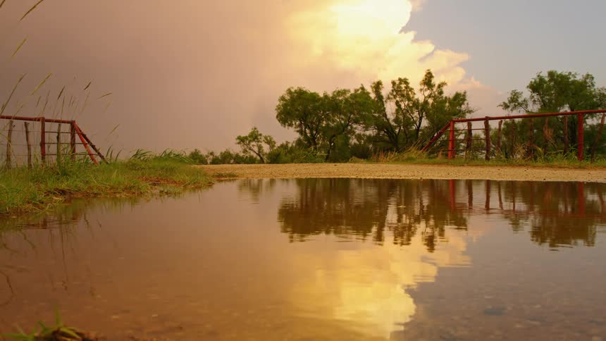 Reflection of a massive supercell thunderstorm at sunset in a puddle with a red cattle gaurd in the background