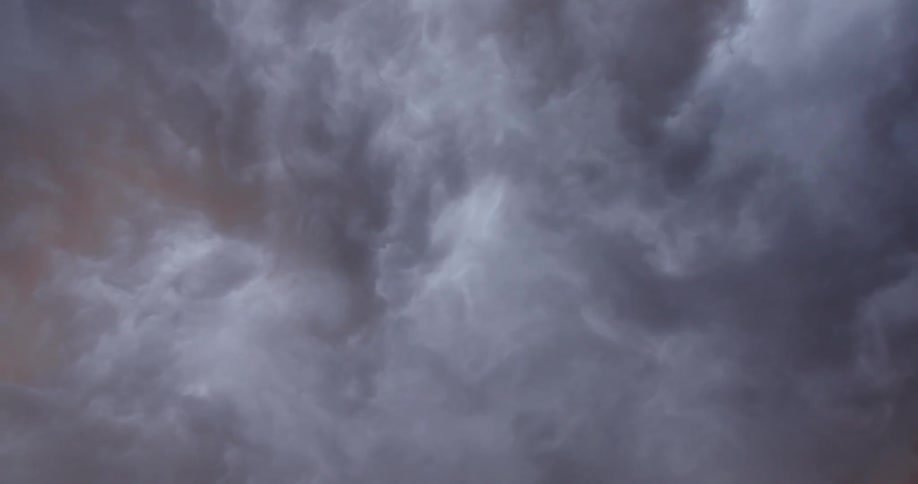 Time lapse looking straight up at rolling and boiling clouds as the sky shifts from purple to golden light as the sun sets
