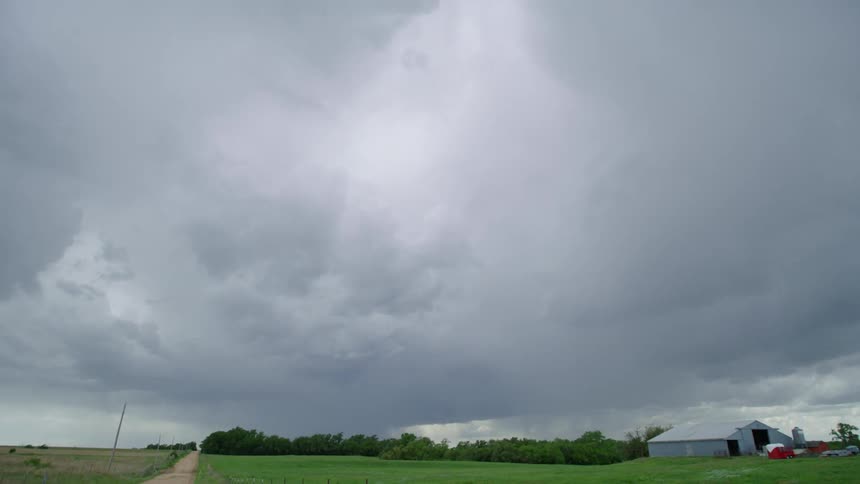 Time lapse of a severe thunderstorm moving past a rural farm in Nebraska as a car drives down a dirt road towards camera