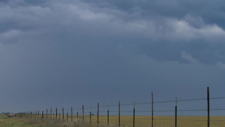 Time lapse shot of severe thunderstorm blue and ominous clouds rolling and boiling in front of a long barb wire fense