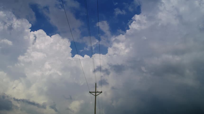 Time lapse with power lines punctuatomh large cumulous nimbus clouds billowing and expanding high into the atmosphere