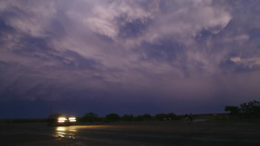 The camera pans right in this real time after sunset blue hour shot of a beautiful supercell thunderstorm with large bolts of lightning and a car driving by
