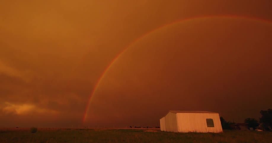 Wide time lapse of a brilliant post storm sunset sky as a giant rainbow arcs across the magic hour red sky