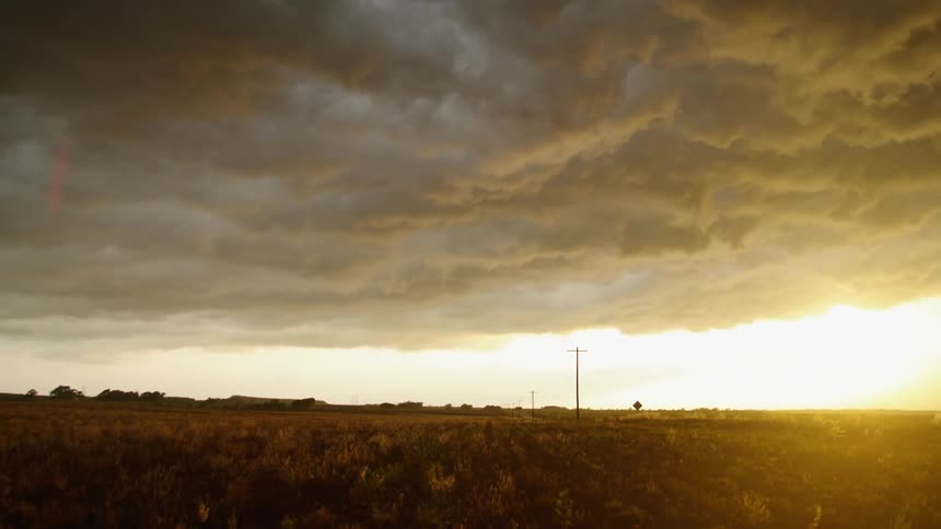 Time lapse as a massive storm moves past the camera revealing a low hanging and bright golden sun as calm prevails after the storm