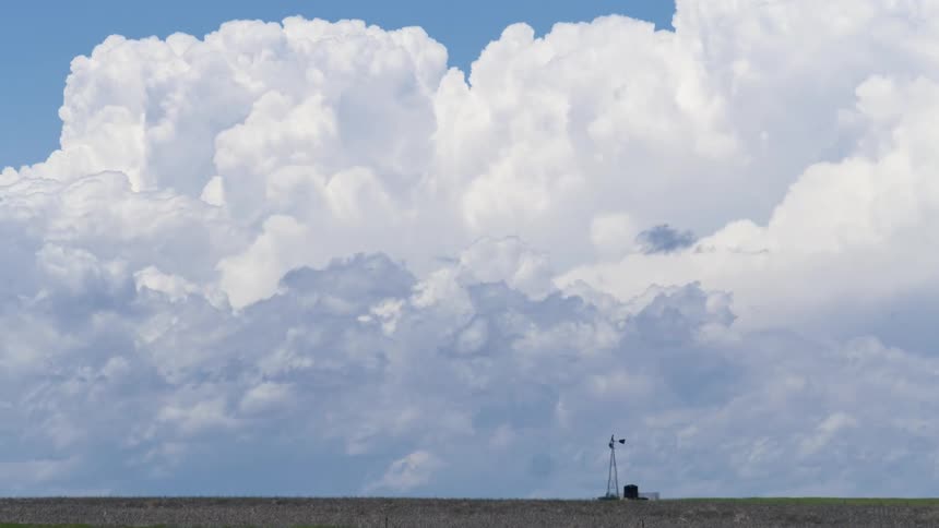 Super wide time lapse of a grassy field with dirt with a windmill blowing in the wind with the sky and clouds in the background