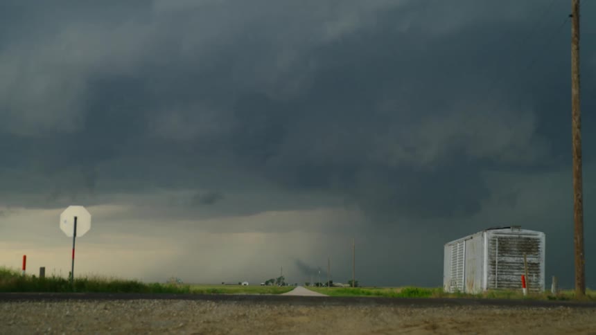 Time lapse of a spin up tornado in a rotating supercell severe thunderstorm while a man photographs the storm and several cars rush by