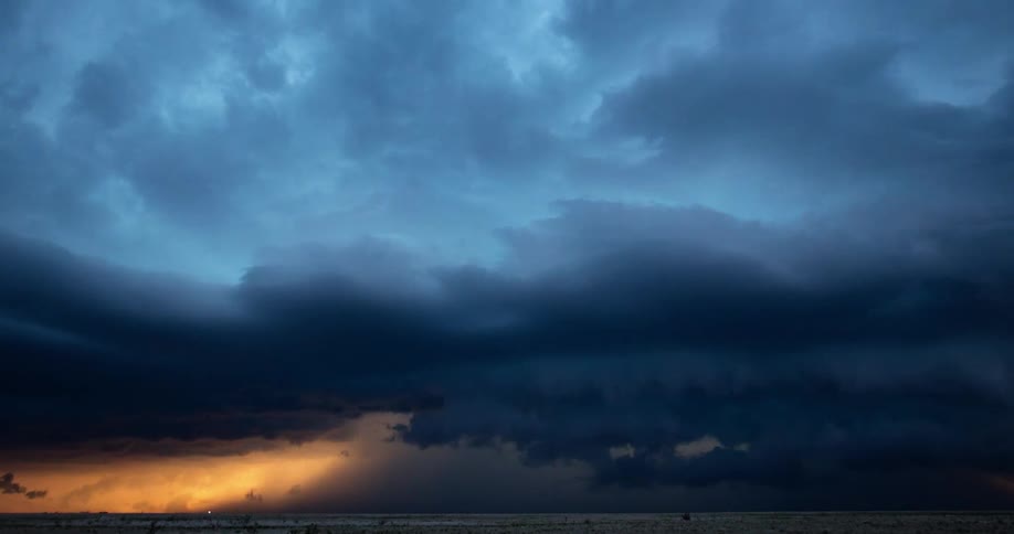 Epic super wide time lapse shot at sunset of an arching and ominous supercell thunderstorm approaching the camera with contrasting blue and golden light hues before overwhelming the camera at the end