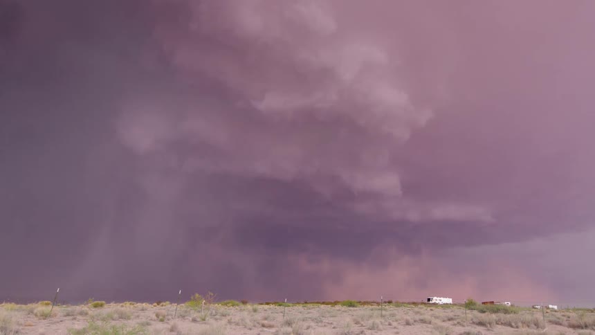 Time lapse of a severe thunderstorm rotating purple over the arid desert land of New Mexico with downdraft winds blowing tan sand out of the frame
