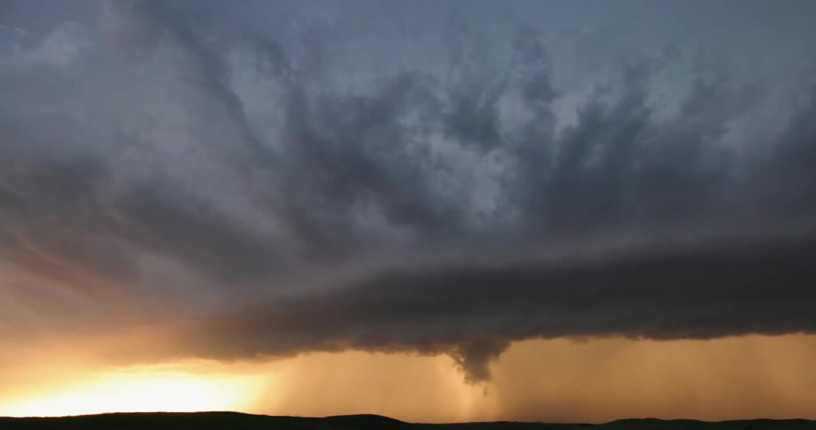 Slow pan left to right of a massive severe thunderstorm with lightning flashing during purple and blue golden hour sunset light