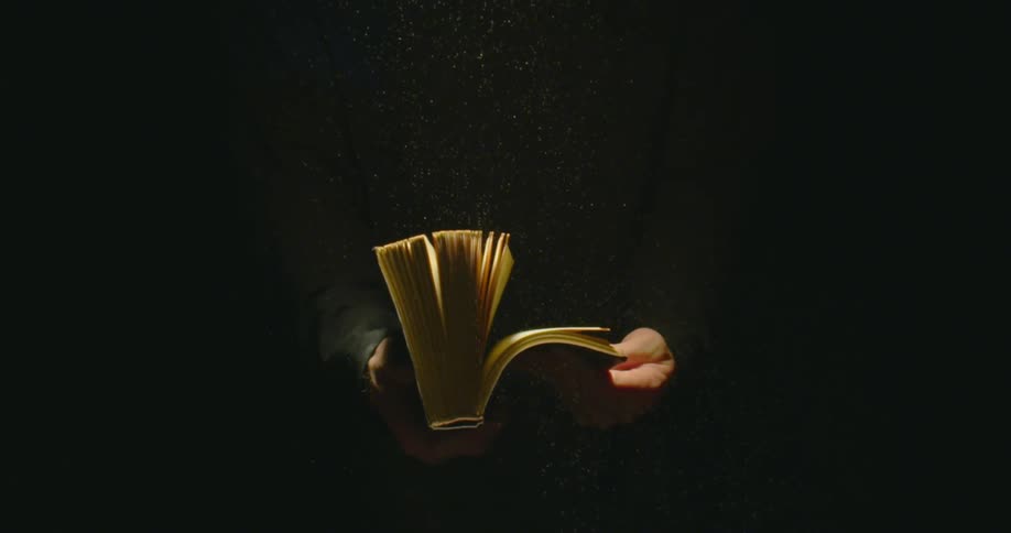 Pages of a book being flicked on the hands of a person in a dark room