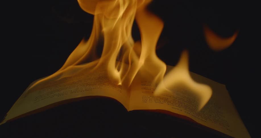 Yellow flames burning the pages of an open book in a dark room