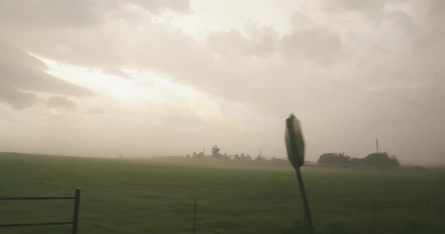 A rural stop sign blowing in the wind during a severe thunderstorm as the car drives by showing the intensity of these supercell severe storms