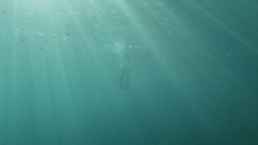 A lone person attempts to stay afloat at the surface of the ocean on a sunny day