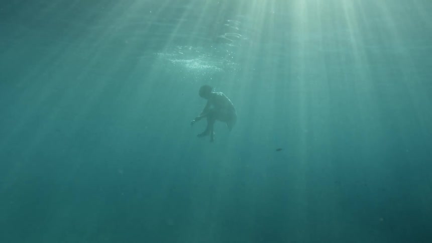Woman flips underwater creating bubbles while sunlight streams down in beams with a fish swimming by