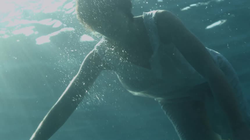 Woman with short hair and a white dress swims underwater