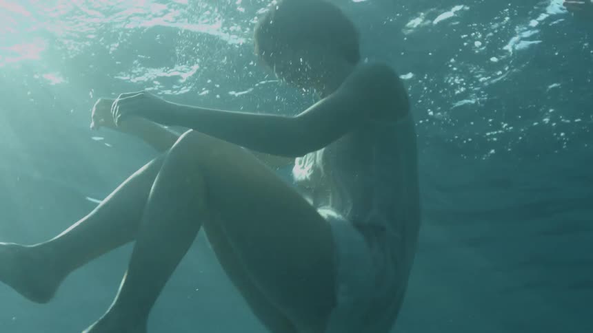 A woman in a dress floats to the surface of the water she is under