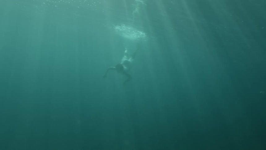 Steams of sunlight shine down on a woman swimming just below the surface of the ocean