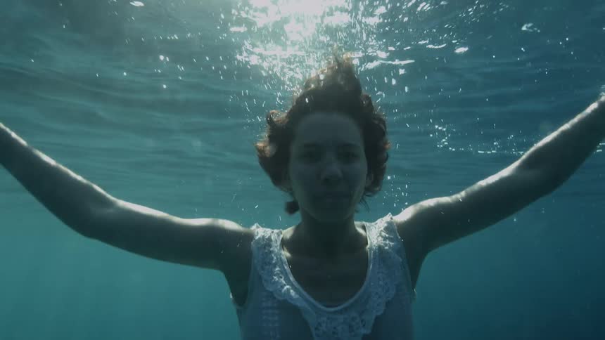 A woman with a white dress swimming underwater with bubbles
