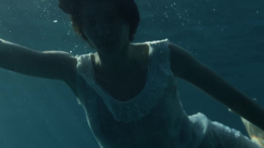 Girl wearing a white dress floating under the surface of the clear blue ocean waters