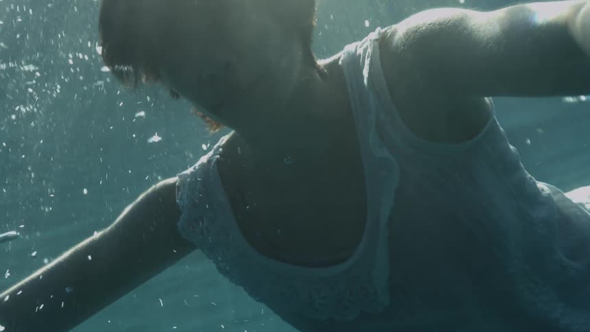 Woman with short hair and a white dress swims underwater