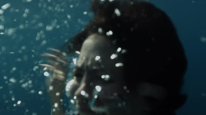 A woman with a white dress struggling underwater with bubbles