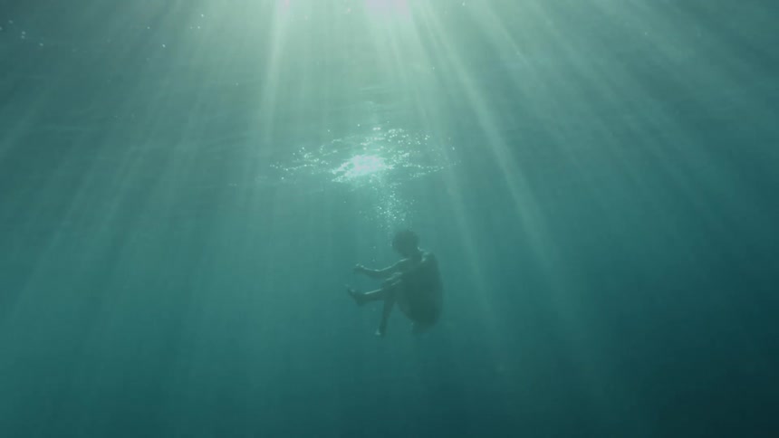 Woman with a white dress swims underwater as the sun shines brightly