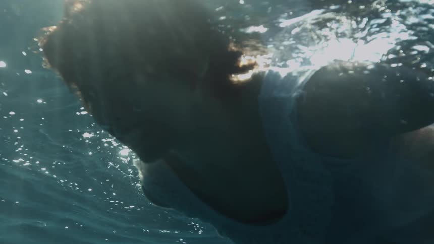 A woman in a nightgown holds her breath while floating underwater