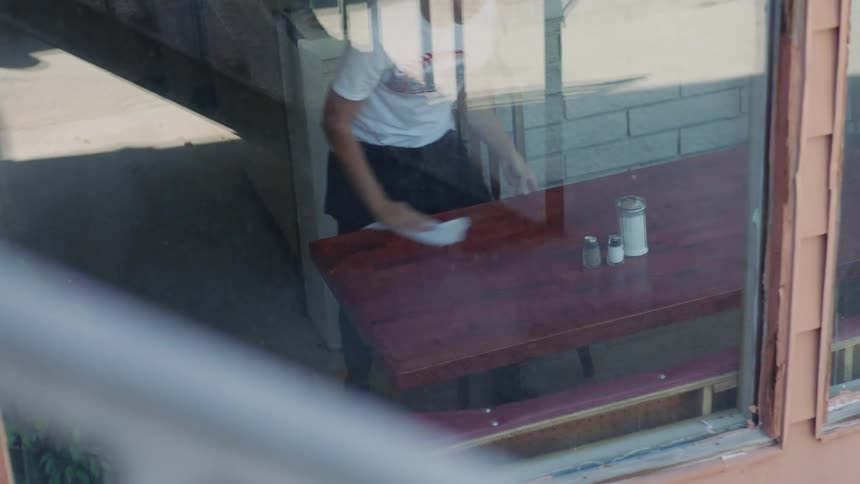 Waitress with a white shirt and black apron cleans a table with a damp towel in the restaurant