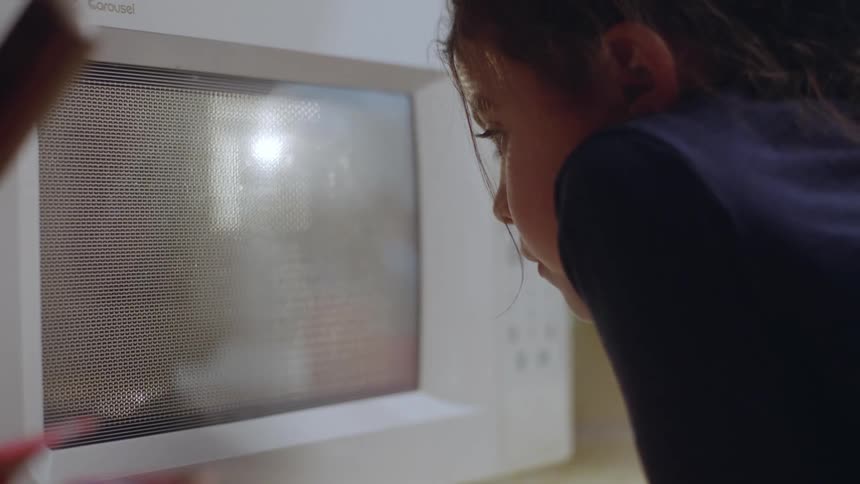 A child watching food cooking in a white microwave