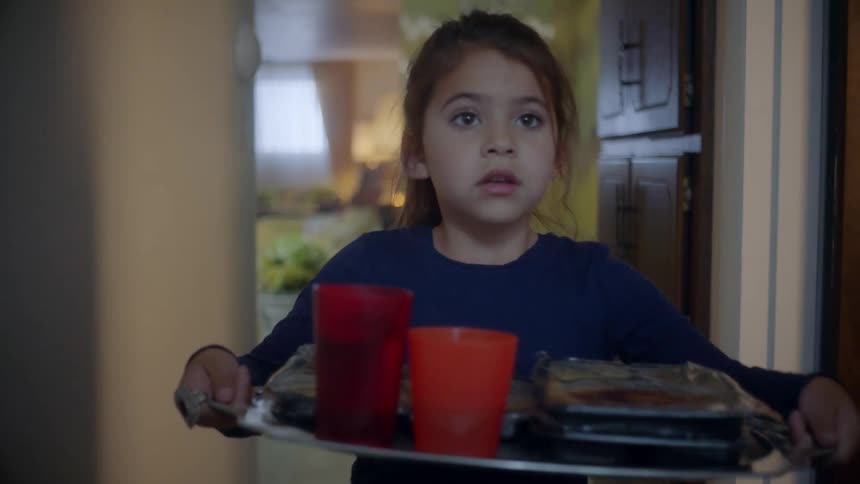 Young girl walks down hallway carrying tray with two cups and a microwave dinner