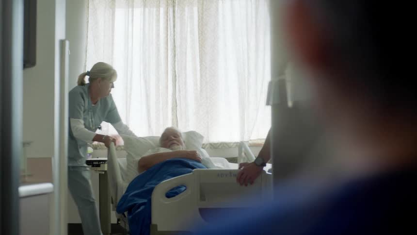 Elderly man on a hospital bed carried by nurses into a room